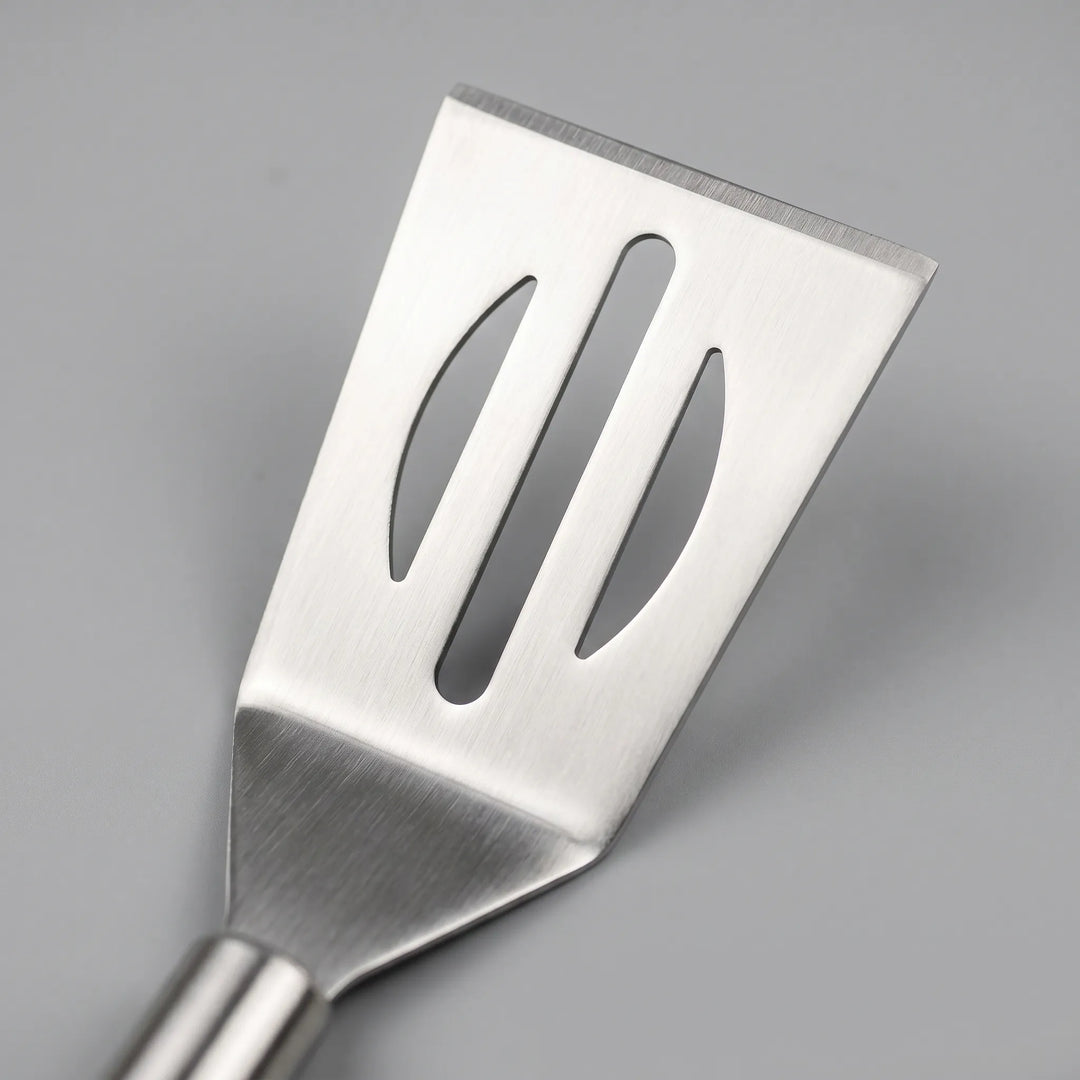 Close-up of a stainless steel grilling spatula, tongs, and fork from a 3-piece BBQ tool set with ergonomic long handles.