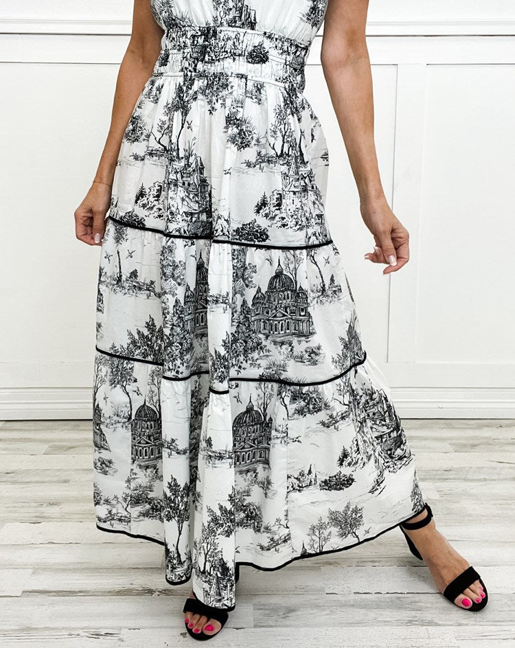 Woman wearing a flowy classic toile maxi dress. Elegant v-neck, smocked waist, perfect for a summer day.