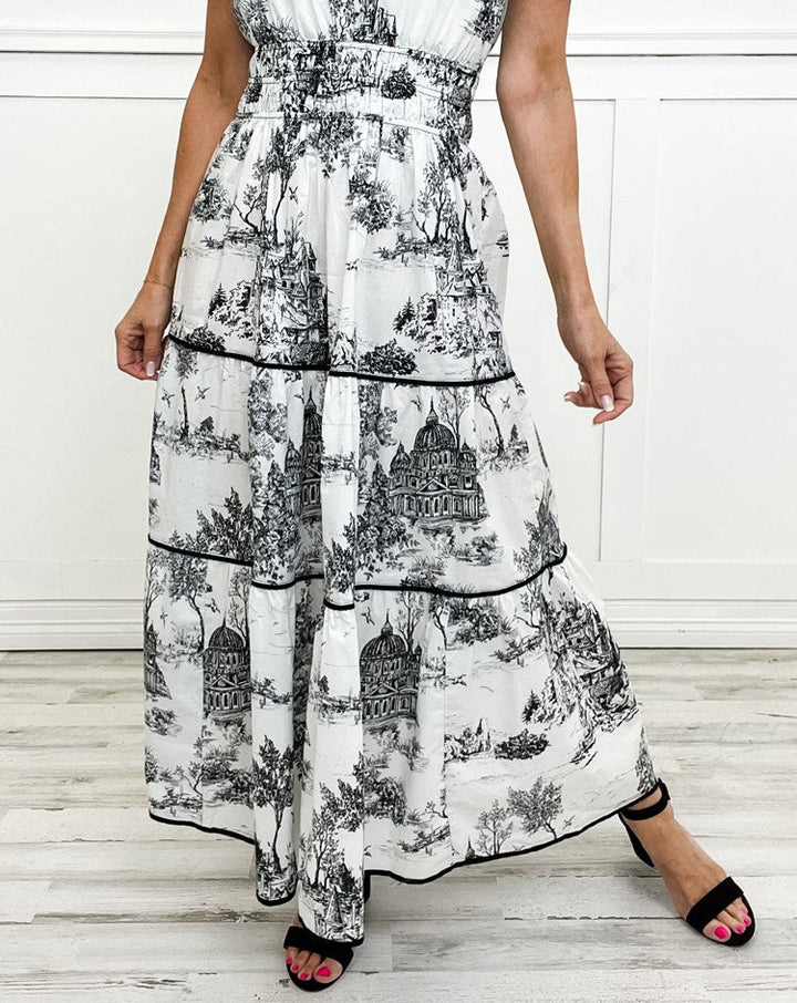 Woman wearing a flowy classic toile maxi dress. Elegant v-neck, smocked waist, perfect for a summer day.