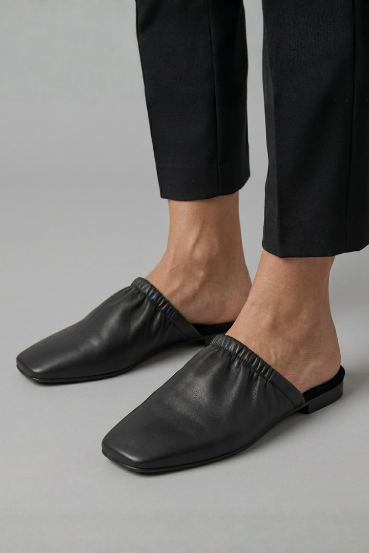 Chic black women's slip-on mules featuring a sophisticated cap toe, versatile for both casual and dressy outfits.