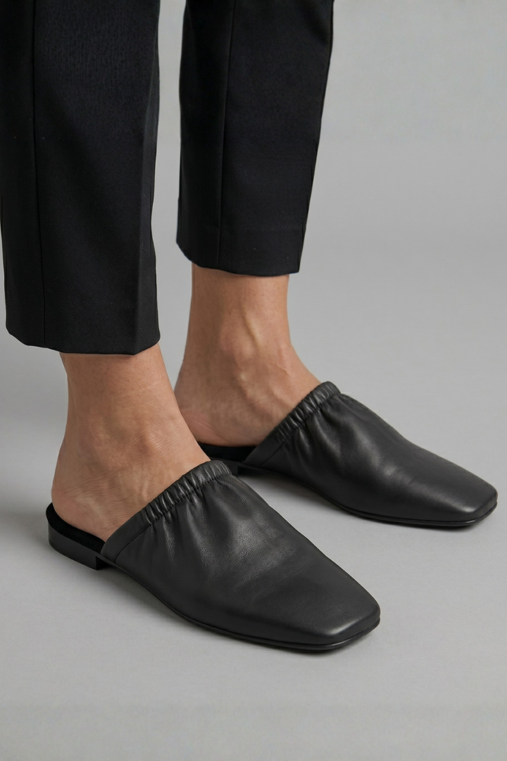 Women's fashion black cap toe slip-on mules. Comfortable, elegant flat shoes for casual everyday wear.