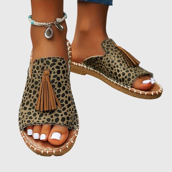 Pair of women's comfortable flat sandals, easy slip-on style with trendy tassel detailing, summer footwear.