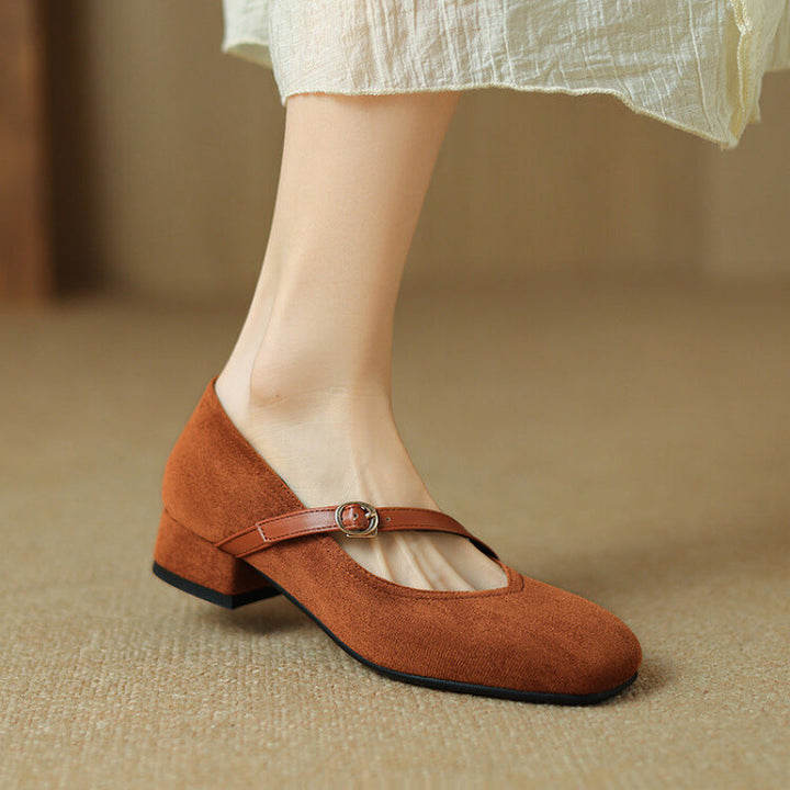 Close-up of the buckle strap on women's tan suede block heel pumps, highlighting detail.