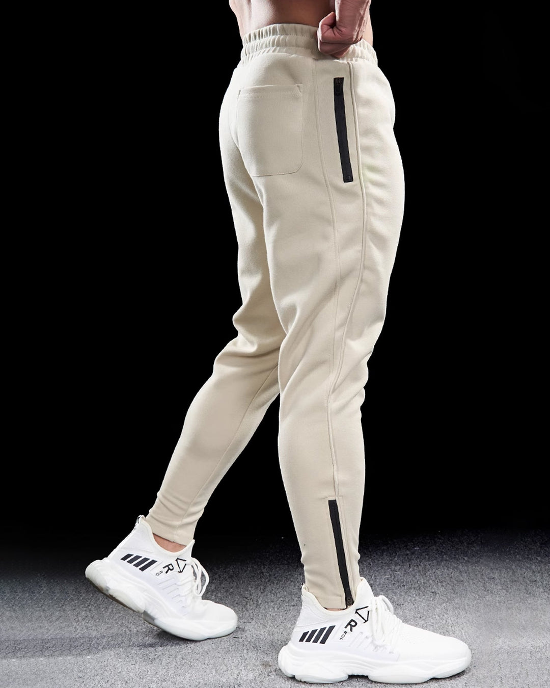 Studio shot of men's tapered track joggers in a neutral tone, featuring zippered hems for a custom fit.
