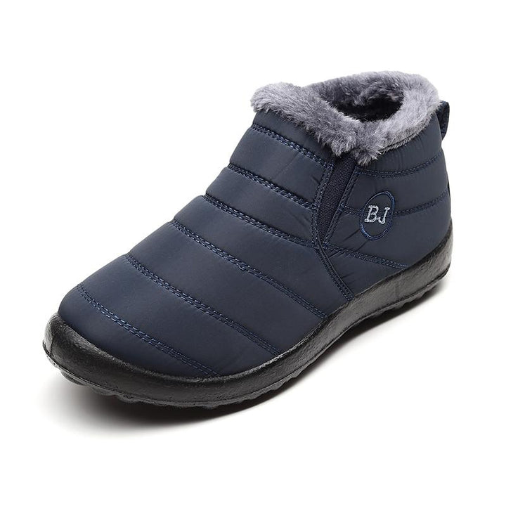 A man wearing black waterproof snow boots, walking outdoors in a snowy environment. Practical winter footwear.
