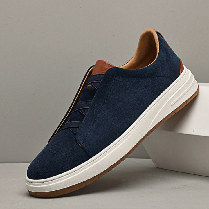 Close-up of a men's blue suede slip-on sneaker, showcasing the soft texture and detailed stitching.