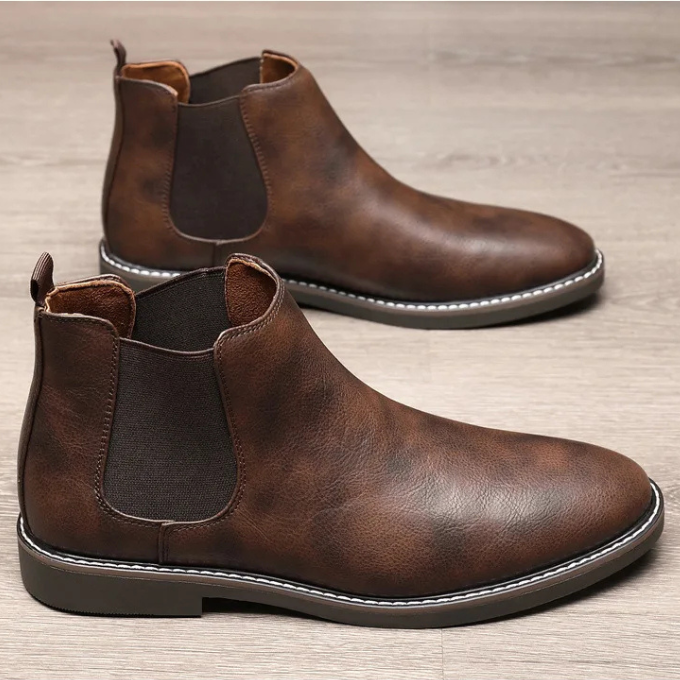 Close-up of men's brown leather Chelsea boot, intricate stitching and texture detail.