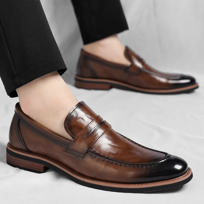 Close-up of a men's polished brown leather penny loafer, showcasing stitched detailing