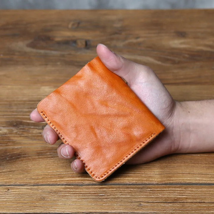 A hand holding a men's full-grain leather bi-fold wallet, demonstrating its ergonomic and slim fit.