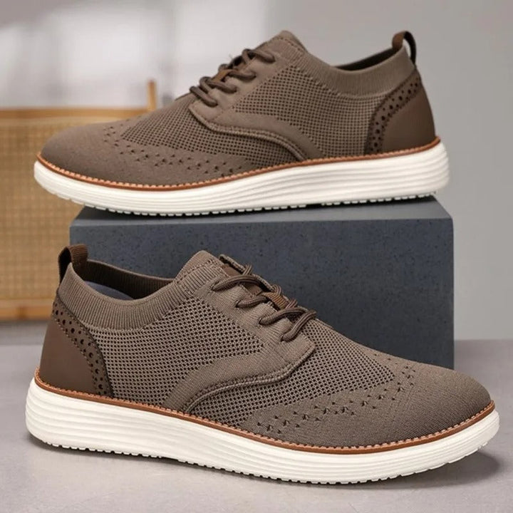 Stylish men's hybrid dress shoes, a blend of formal wingtip and casual sneaker, in a dark color.