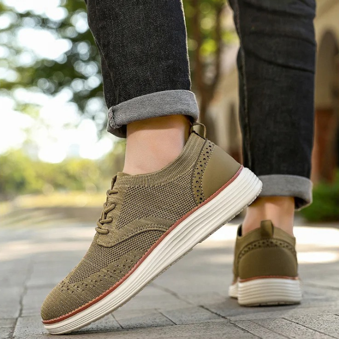 Close-up of a men's hybrid dress sneaker showing the intricate wingtip detail and flexible knit material.