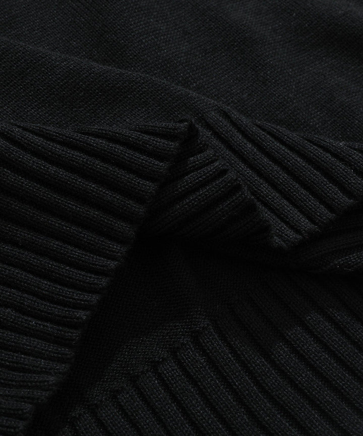 Full shot of a man wearing a black ribbed mock neck half-zip sweater, a staple men's apparel