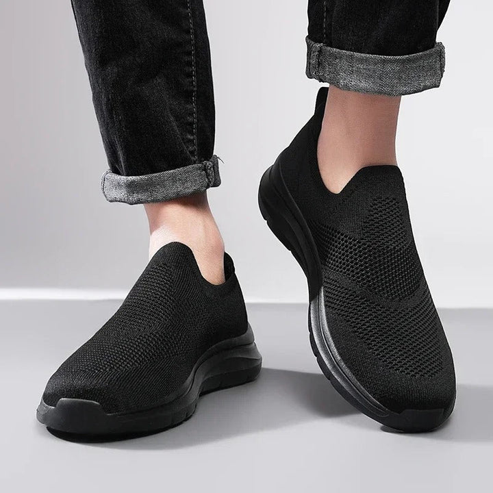 Side view of black unisex knit slip-on sneakers, highlighting the breathable upper and foam sole.