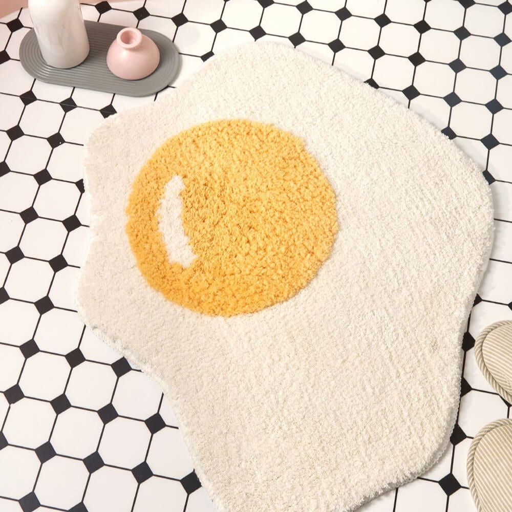 Whimsical fried egg shaggy bath mat. Soft, absorbent, non-slip, machine washable. Perfect playful home decor.