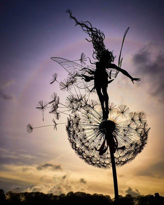 Whimsical metal fairy with lifelike dandelion stakes, ideal for enchanting garden decor, adding magic to outdoor spaces.