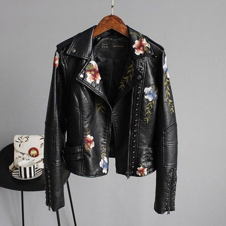 Women's black faux leather biker jacket with vibrant floral embroidery & studded details on lapel, zip-up style.
