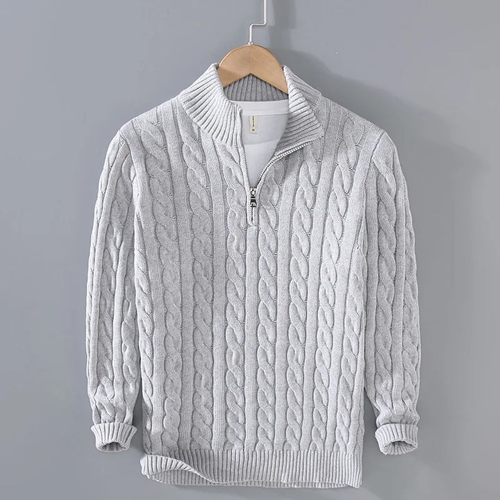 Close-up of the intricate cable knit pattern on a women's half-zip sweater in a light color.