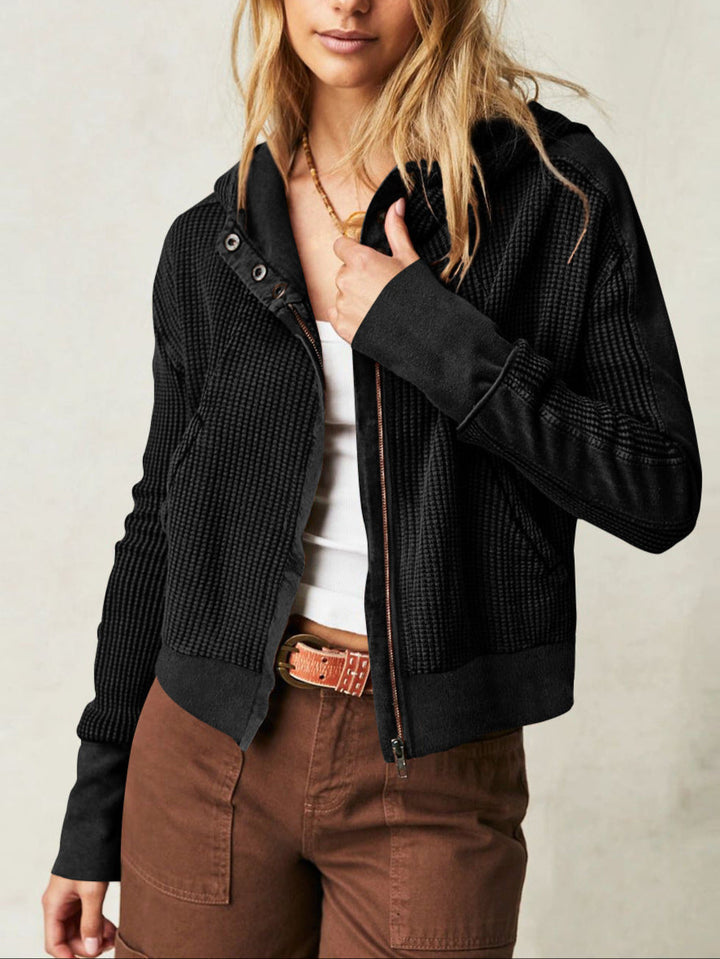 Woman wearing a black cropped waffle-knit zip hoodie, front view, casual apparel