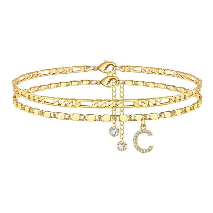 Close-up of a women's gold initial anklet featuring a clear crystal charm, personalized jewelry